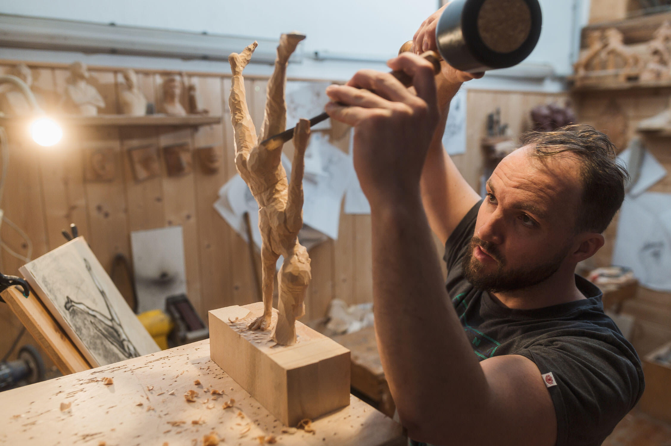 genaues Arbeiten am Schnitzen einer Figur. im Hintergrund ist die Skizzenzeichnung zu erkennen